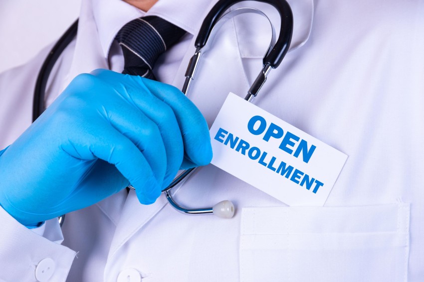 Doctor holding up "Open Enrollment" sign with stethoscope around neck.